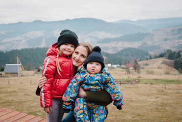 Mom, daughter, hug son enjoy time together. Active weekend travel concept in mountains. Mother embraces baby and kids on a terrace on an autumn day. People stand in backyard of country house.