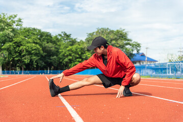 Young Asian man stretching his leg warm up before workout outdoor running track background. The man in sportswear exercises outside in the morning for health and wellbeing.