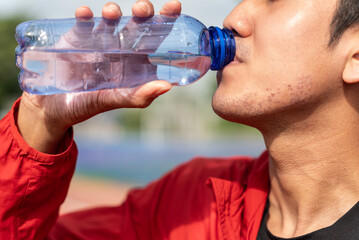 Close up of young asian man drinking water from bottle after running with running track background,...