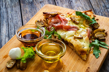 Slice of pinsa Romana with ham, mozzarella cheese and white mushrooms on wooden table

