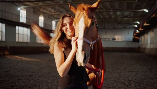 Smiling woman strokes horse waving long tail at farm