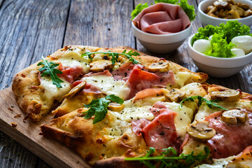 Pinsa Romana with ham, mozzarella cheese and white mushrooms on wooden table

