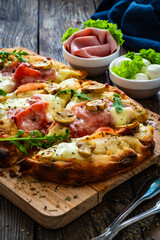Pinsa Romana with ham, mozzarella cheese and white mushrooms on wooden table
