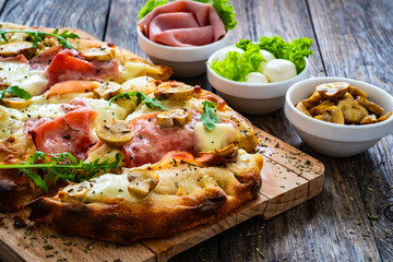 Pinsa Romana with ham, mozzarella cheese and white mushrooms on wooden table
