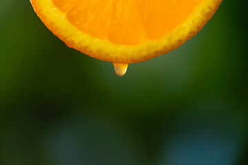 Drop of juice dripping from a slice of orange on a blurry green background, macro photography. Fruit background