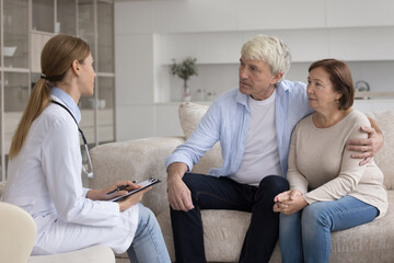 Obraz premium Young doctor visiting happy mature older couple of patients at home, talking to positive husband and wife, explaining prescription, telling good examination news, giving medical consultation