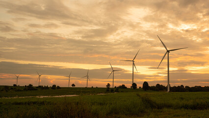 Fototapeta premium Wind turbines generate electricity in a rural area during sunset. Windmill farm on mountain with sunset sky. Wind energy, renewable energy, Green technology.
