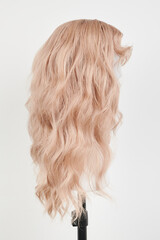 Naklejka premium Natural looking blonde wig on white mannequin head. Long hair on the plastic wig holder isolated on white background, side view.