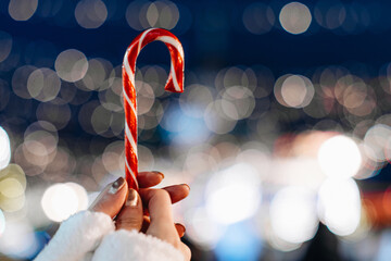 Female hands holding red white cane sweet candy lollipop against the background of blue silver...