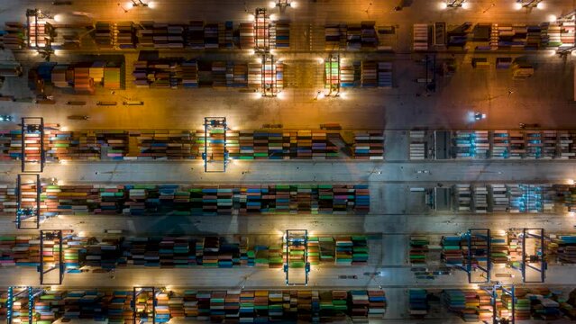 Aerial top down time lapse view of rows of cargo containers and trucks in a commercial harbour during dusk