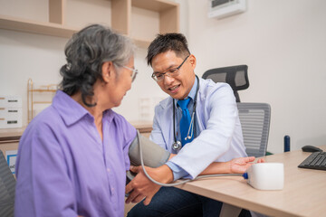 Obraz premium Asian caregiver doctor using digital pressure gauge measuring blood pressure of elderly woman patient. Young female nurse in uniform gives consultation during home visit. Medical and health concept.
