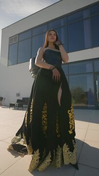 Beautiful Princess Woman with Crown on her Head and Black Dress with Gold Patterns Stands near Large Chess Piece Background Luxury Villa. Fashion Model Poses in Image Historical Queen. Vertical Video
