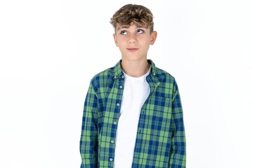 Caucasian teen boy wearing  green plaid shirt over white background looking aside into empty space thoughtful