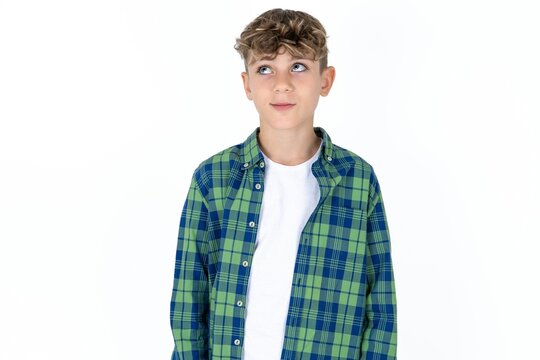 Caucasian teen boy wearing  green plaid shirt over white background looking aside into empty space thoughtful