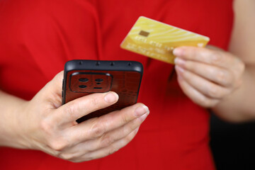 Woman in red dress holding smartphone and credit card in hands. Concept of online payments,...