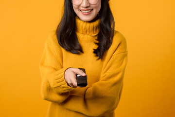 A content young woman in a yellow sweater holding a remote control, enjoying leisure time in her...