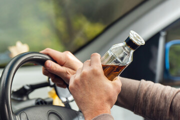 The driver is sitting behind the wheel and holding a bottle of alcoholic drink. Breaking the law and drinking alcohol while driving