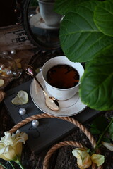 a cup of tea stands on a stack of books, next to a flower, behind an antique mirror