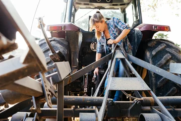 Cercles muraux Tracteur Young female mechanic in a farm repairing tractor