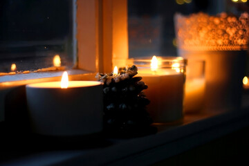 Lit candles and Christmas decorations on the window sill at night. Hygge at home. Selective focus.