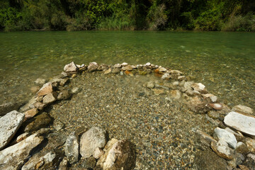 Río de agua transparente delante de una presa con piedras en circulo dentro del agua 