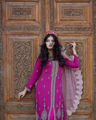 A girl in a national pink outfit near an ancient wooden door of a house