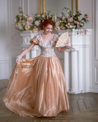 Red-haired girl in a vintage dress dances at a ball and smiles