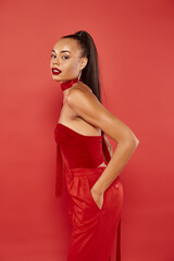 Fototapeta premium beautiful african american model in red strapless top and pants posing with hand in pocket