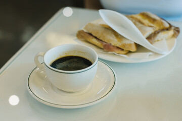 Cup of black coffee and a sandwich on a table in a cafe.