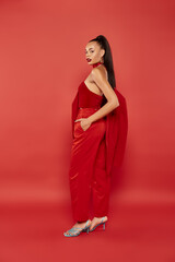 full length of elegant african american woman with ponytail posing in red suit with hand in pocket