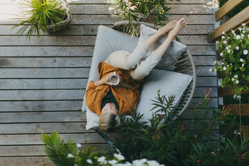 Top view of woman relaxing in the garden, drinking coffee and lying on patio chair. Mother having moment to herself while her child is sleeping. - obrazy, fototapety, plakaty