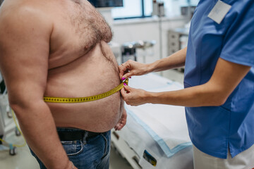 Female doctor measuring waist of overweight patient using tape measure. Obesity affecting...