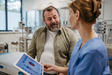Female doctor consulting with overweight patient, discussing test result in doctor office. Obesity affecting middle-aged men's health. Concept of health risks of overwight and obesity. - obrazy, fototapety, plakaty
