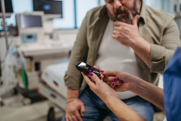 Doctor checking blood glucose level using a fingerstick glucose meter, waiting for results from...