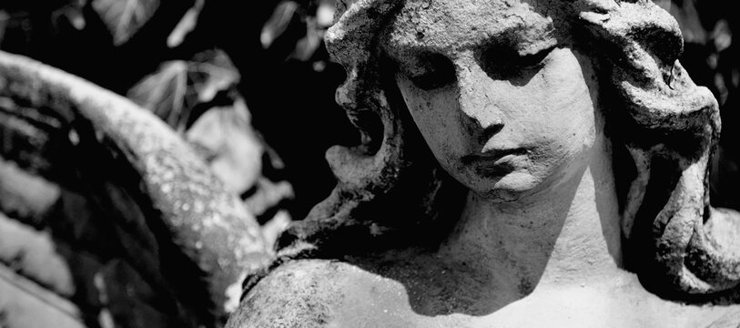 Black and white image of ancient stone statue of angel with a sweet expression that looks down