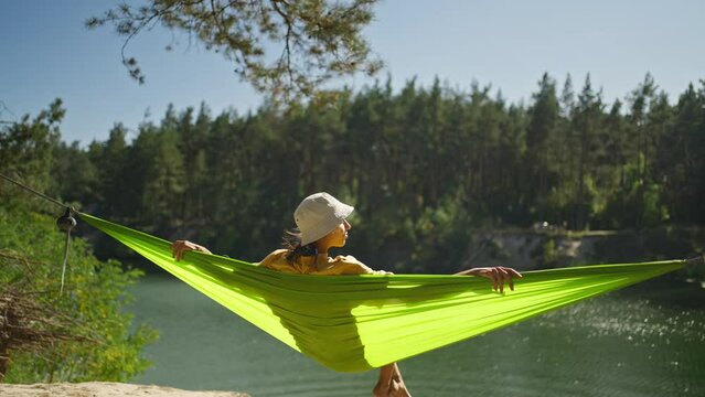relaxed woman swinging in hammock on mountain lake shore in forest. wanderlust, summer vacation, travel outdoors, active leisure. happy girl is resting in a summer forest on a green hammock