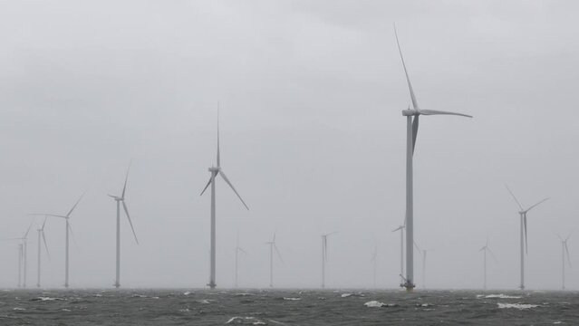 Large offshore windmills, turbines for alternative green, renewable energy, electricity, just of the Dutch coast in high winds, stormy weather, storm. High waves, dramatic. IJsselmeer, the Netherlands