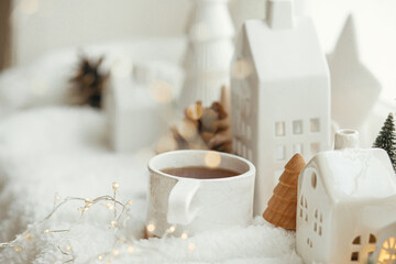 Fototapeta na wymiar Cozy winter still life. Stylish cup of tea with modern christmas decoration, pine cone, wooden star and tree, golden lights on soft warm blanket on windowsill. Merry Christmas and Happy holidays