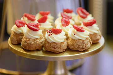 Candy bar, delicious little cakes decorated with cream, strawberries are at wedding event, party.