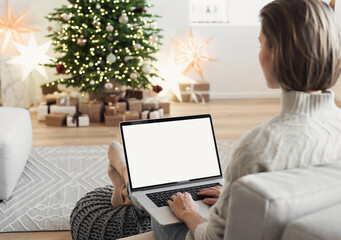 Young woman using laptop computer with blank empty mockup screen during Christmas holidays at home, Online shopping at winter holidays, ordering Christmas gift, Website template - obrazy, fototapety, plakaty