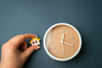 A miniature house in hands and a clock. Mortgage and loan concept. Temporary rental housing and...