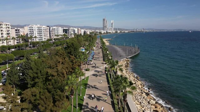 Aerial view of people walking in beautiful green park, along seafront promenade, with the skyline of Lemesos (Limassol) in the background, urban landscape in Cyprus Europe