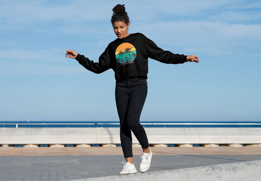 Mockup of woman wearing customizable sweatshirt by low wall, arms out