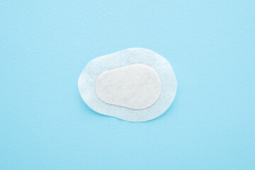 White sticking plaster for eye covering on light blue table background. Pastel color. Closeup. Top down view.