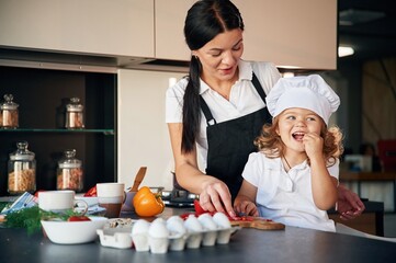Giving a taste to pepper. Mother with her daughter are preparing food on the kitchen