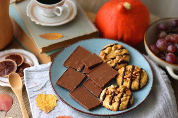 Cup of tea or coffee, plate with desserts, dried oranges, bowl of grapes, scented candles, vintage books, pumpkins and autumn leaves on the table. Autumnal hygge. Selective focus.