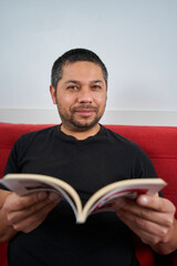 Man on Sofa Holding Book, Engaging with Camera