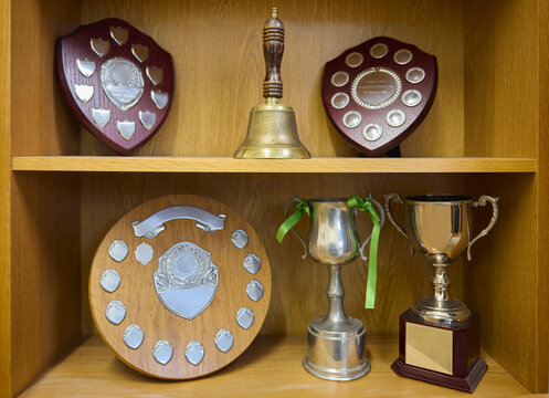 Trophies For Achievement  On Display In Cabinet With Old Fashioned School Bell