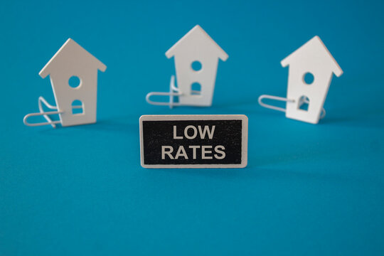 Low house rates symbol. Concept red words Low rates on wooden board near miniature houses. Beautiful blue background, copy space. Business and low house rates concept.