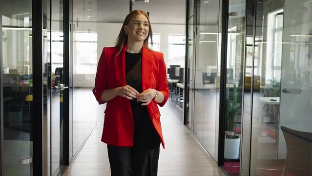 A confident businesswoman in striking red attire gracefully navigates the hallways of a modern startup space, exuding style and professionalism.